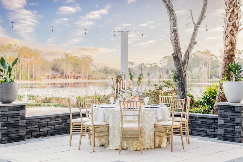 Round reception table with gold chiavari chairs on the paver terrace at Fern Oak Estate, string lights above and the lake beyond