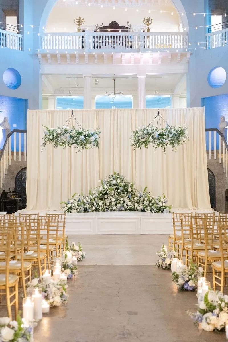 Lightner Museum wedding ceremony with cream draping and suspended florals under deep-blue uplighting
