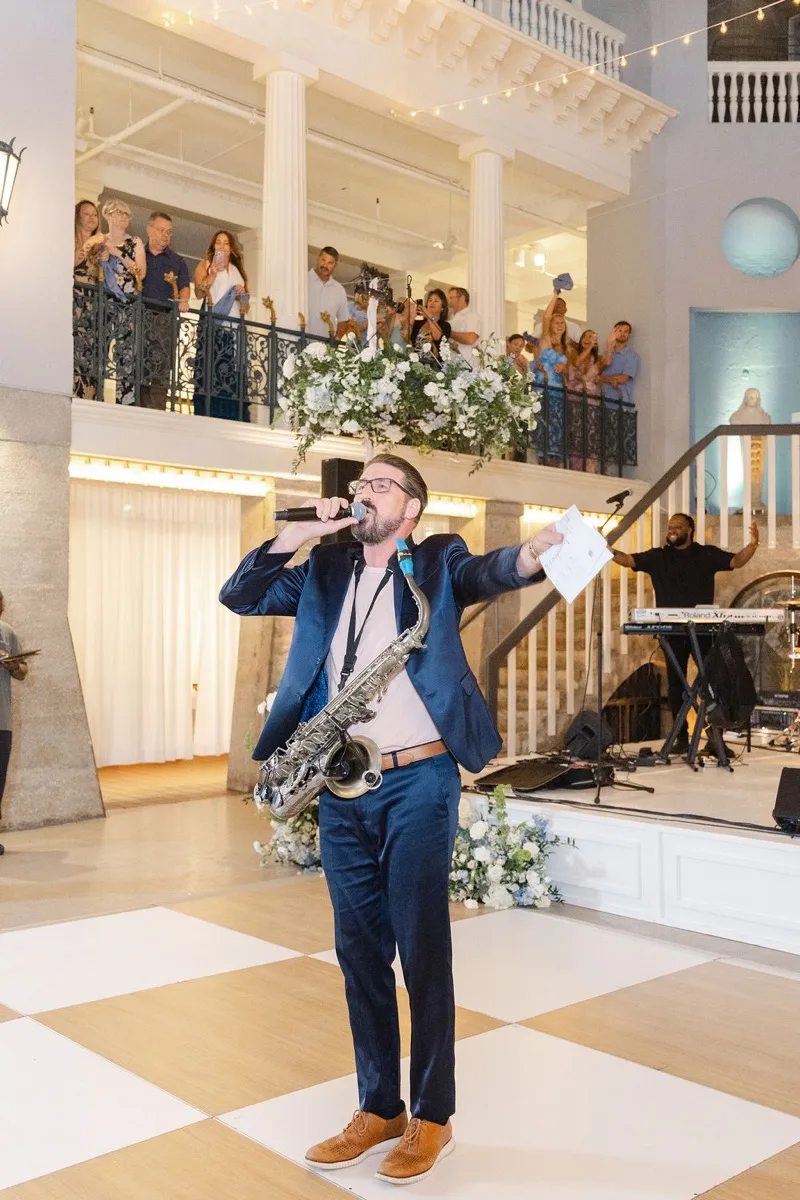 Wedding emcee at Lightner Museum holding a microphone with a saxophone slung across his shoulder