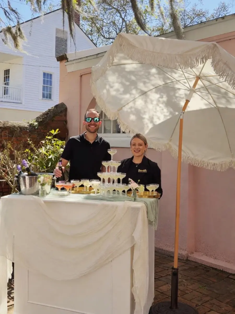 A Maci's Pour bar set up outdoors with a champagne coupe tower, draped linen and bottles chilling on ice