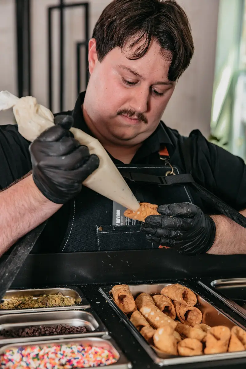 Anthony of That Cannoli Guy piping filling into a cannoli shell over his tray